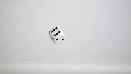 One white dice in super slow motion rebonding on the grey floor - Powered by Adobe