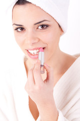 Young woman applying lipstick with a bath robe