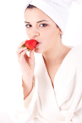 Beautiful woman in a white spa bath robe eating a strawberry