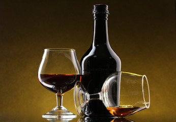 Glasses of brandy and bottle on yellow background