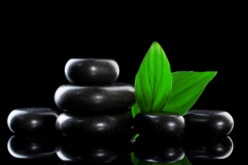 Spa stones and green leaves on black background