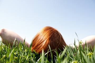 Red haired woman laying in grass looking up