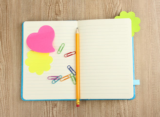 Open note book with stickies and pencil on wooden background
