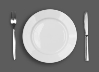 Knife, white plate and fork on gray background