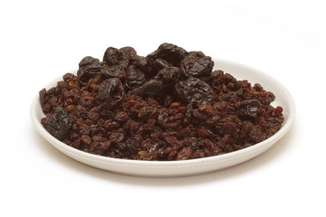Lot of prunes, raisins on round plate isolated on white