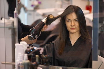 Pretty lady sitting while hairdresser dries her hair