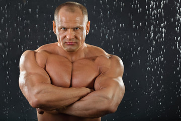 Thoughtful tanned bodybuilder stands in rain inside studio