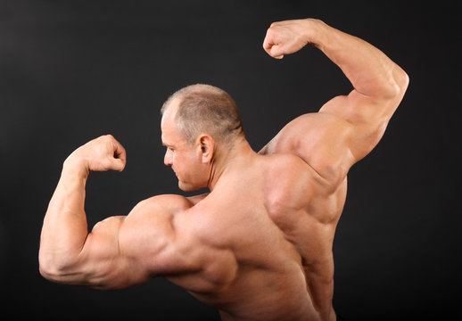 Undressed tanned bodybuilder shows muscles of arms and back
