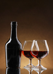 Glasses of brandy and bottle on brown background