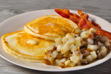 Pancakes, bacon, and hash browns on old vintage wood table