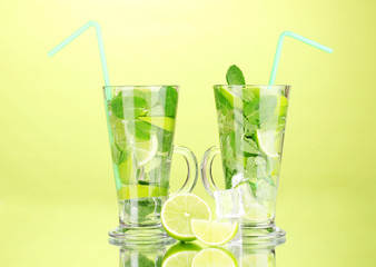 Glasses of cocktail with lime and mint on green background