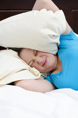 Young woman covering ears with pillow because of noise.