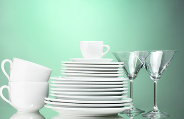 Clean plates, cups and glasses on green background