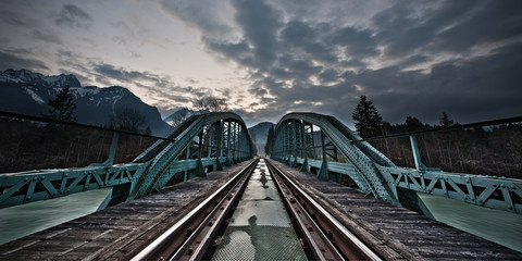 painted framework bridge and rails at sunset with dramatic sky