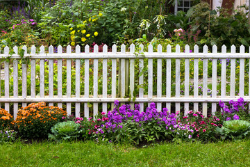 White picket fence surrounded by garden flowers in yard - Powered by Adobe