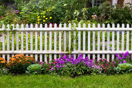 White picket fence surrounded by garden flowers in yard