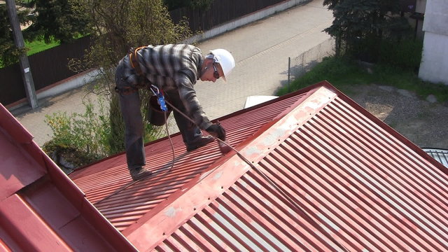 Man paints roof of a private house with safety rope