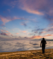 silhouette of the man walking above the clouds on the sunrise