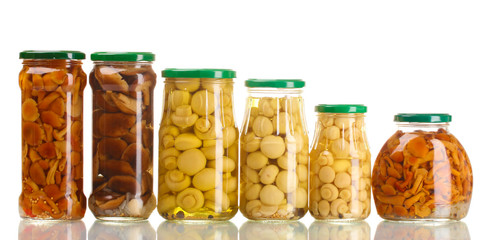 Different glass jars of marinated mushrooms isolated on white