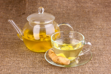 Healthy ginger tea in kettle and cup on sackcloth