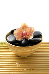 Wooden bowl of stones and orchid on mat