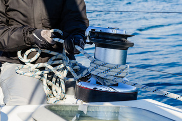 Crew work with genoa sheet rope and winch on sailing boat.