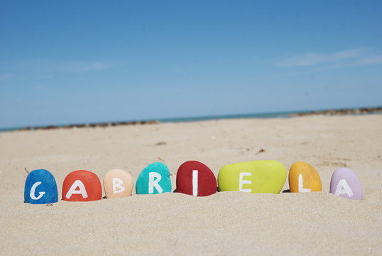 gabriela, female name on colourful pebbles on the sand