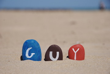 Guy, male name on colourful pebbles on the sand