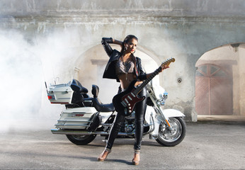 A young Caucasian woman  with a guitar posing near a bike