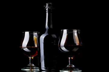 Glasses of brandy and bottle on black background