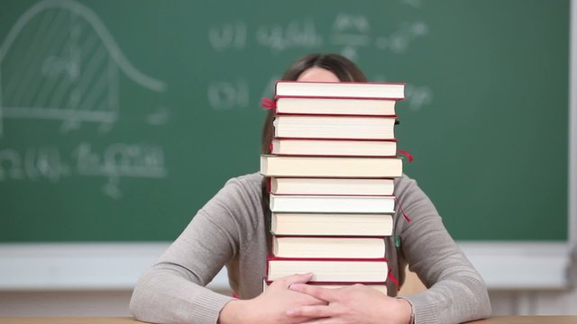 lachende frau schaut hinter schulb&uuml;chern hervor