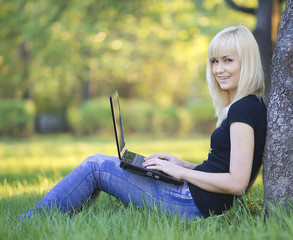 Young woman with laptop sitting on green grass