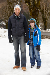 Fototapeta na wymiar Father And Son Walking Along Snowy Street In Ski Resort
