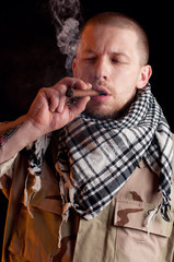 Soldier in combat uniform smoking cigar, dark background