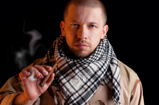 Brawny mercenary smoking cigar, over black background