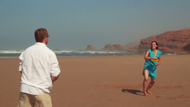 Happy couple having fun with freesby on the beach, slow motion