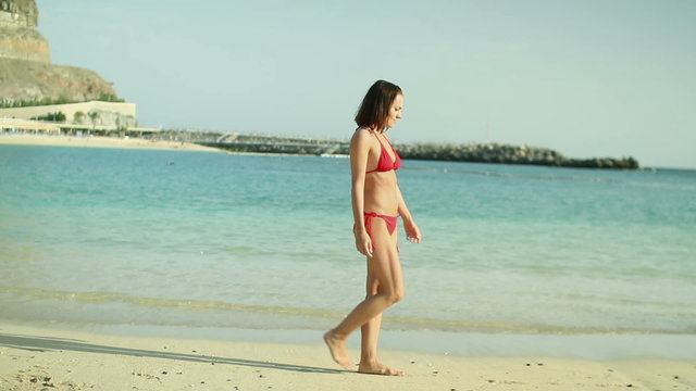 Woman in red bikini walking on the beach, steadicam
