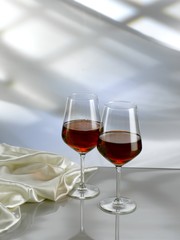 Red wine into two stem glasses on white table