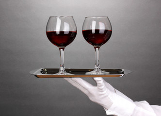 Hand in glove holding silver tray with wineglasses