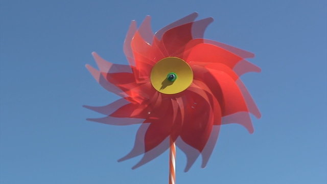 Red pinwheel toy spinning against a vivid blue sky