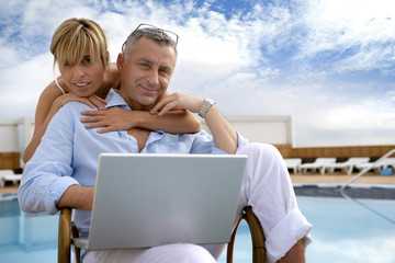Couple using a laptop by the poolside