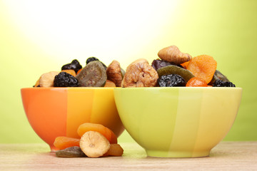 Dried fruits in bright bowls on wooden table on green background
