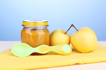 Jar of baby puree with spoon on napkin on blue background