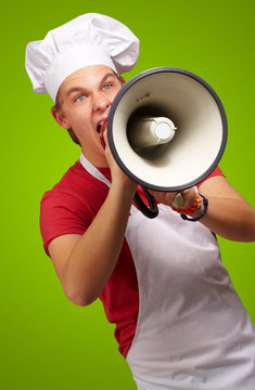 portrait of young cook man screaming with megaphone over green b