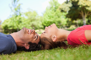 Two smiling friends looking at each other while lying head to he