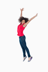 Fototapeta na wymiar Smiling young brunette jumping while raising her arms above her