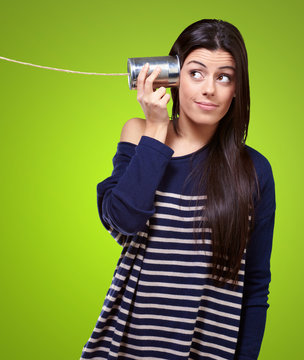 portrait of young woman hearing through a tin can over green
