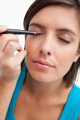 Obraz premium Young woman using an eye pencil to apply make-up