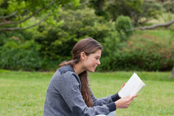 Side view of a young girl sitting cross-legged while reading a b