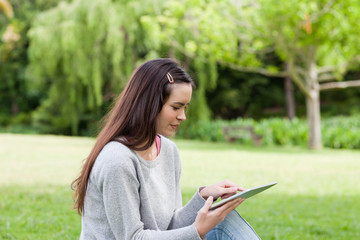 Young relaxed woman sitting in a park while using her tablet pc
